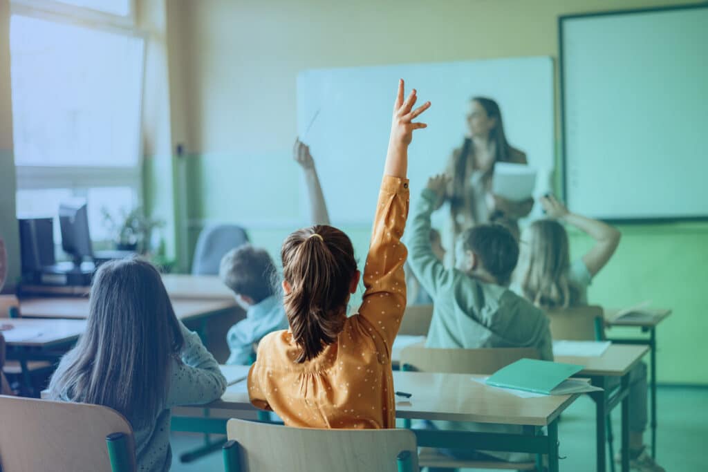 Students raising hands while teacher asking them questions in classroom