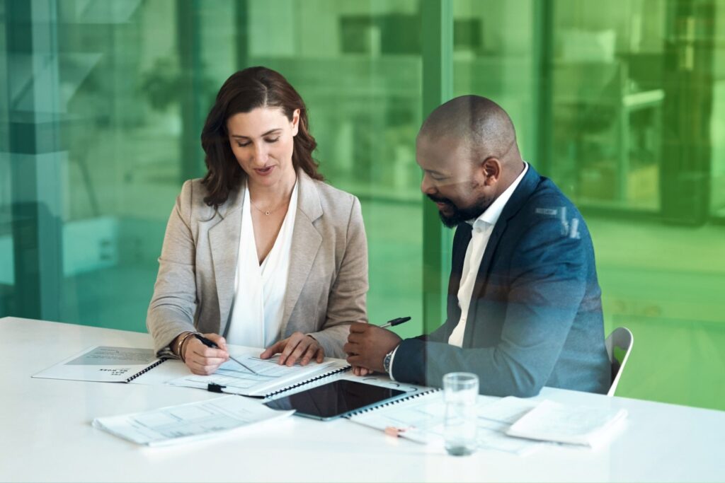 Two colleagues sitting at a desk reviewing documents together in an office