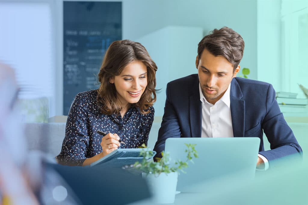 Two colleagues sitting at a desk reviewing documents together in an office