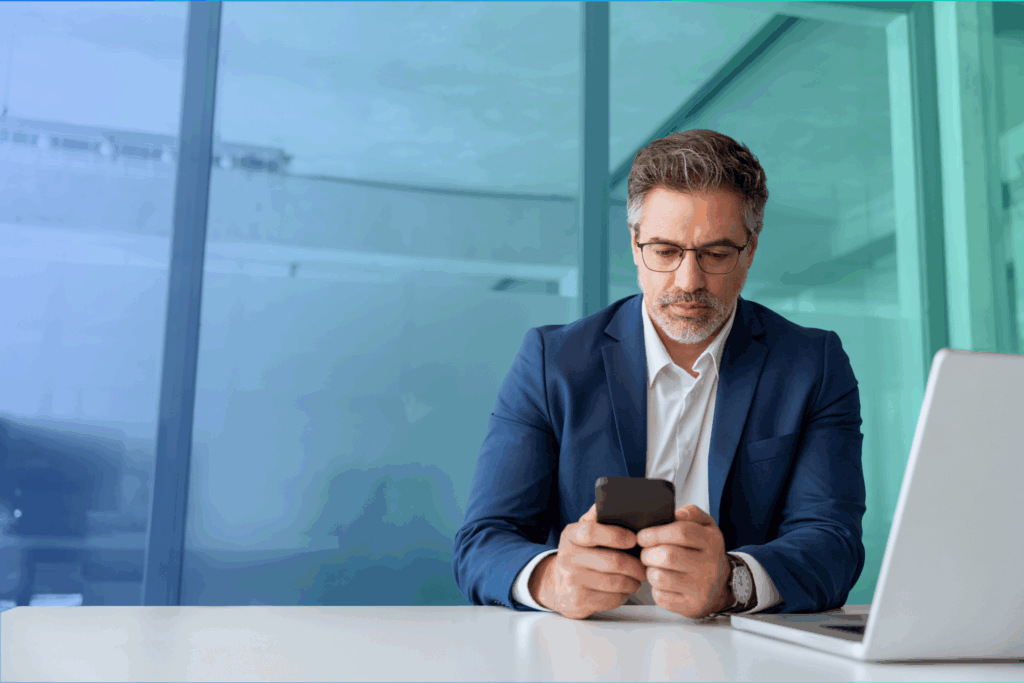 Man in suit sitting in front of laptop while using mobile phone